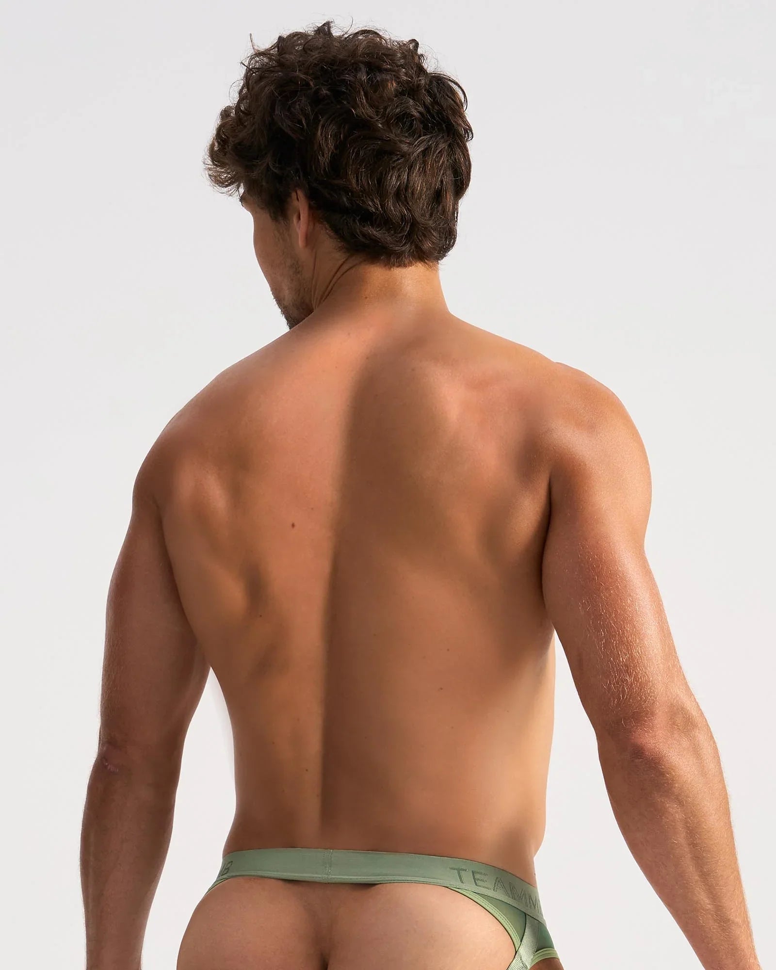 A man wearing olive green low-rise score sheer jock briefs with teal brand name on the waistband front view