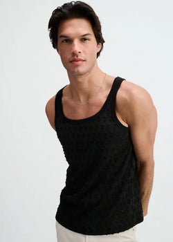 A man wearing a black ST33LE stretch ripped knit tank top with a scoop neckline and subtle distressing throughout.
