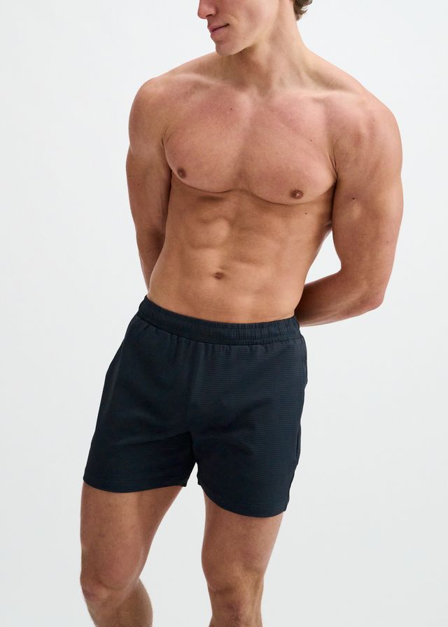 A shirtless man wearing dark blue ST33LE Textured Mesh Stretch Performance Shorts with an elastic waistband.