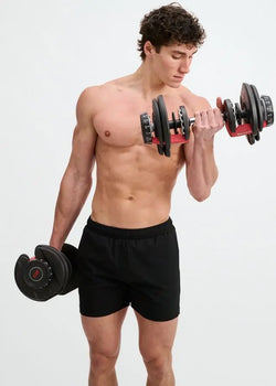 A shirtless man lifts dumbbells wearing ST33LE black textured stretch performance shorts.