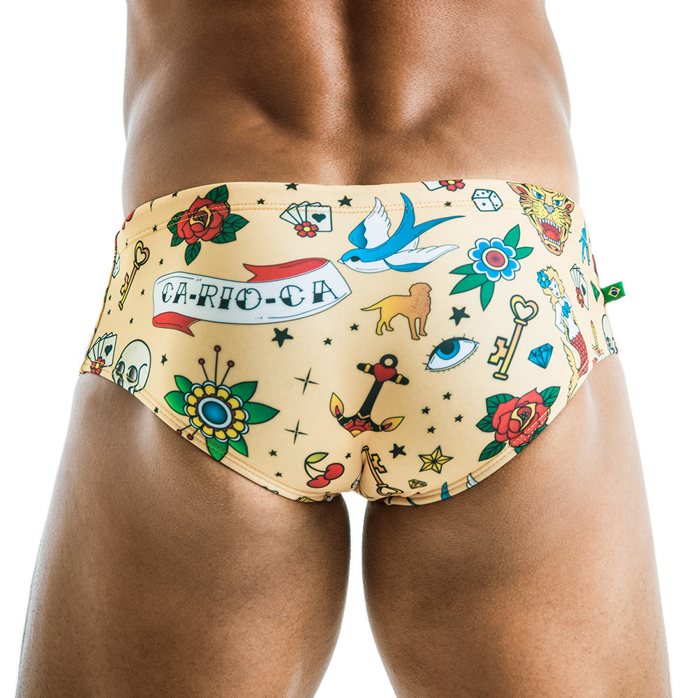 Beige sailor tattoo sunga men’s designer swimwear featuring vibrant red roses blue birds and ca-rio-ca banner print