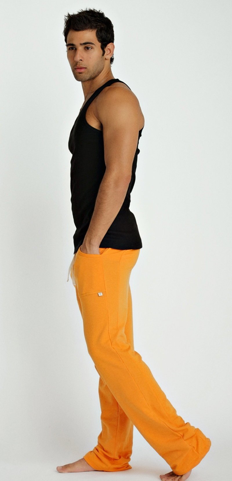 Bright orange loose-fitting pants with a small white logo on the thigh paired with a black sustain tank top