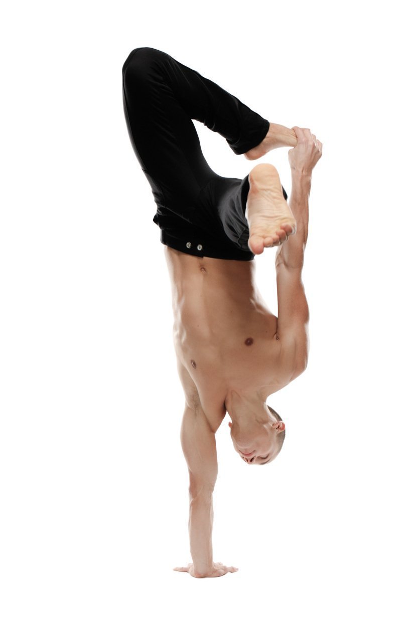 A muscular man performs an acrobatic handstand wearing black tactical urban at home dress pant yoga pants