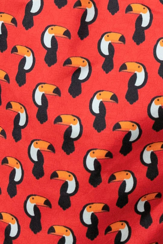 Red toucan print swim short featuring a repeating pattern of stylized black white and orange toucans on fabric