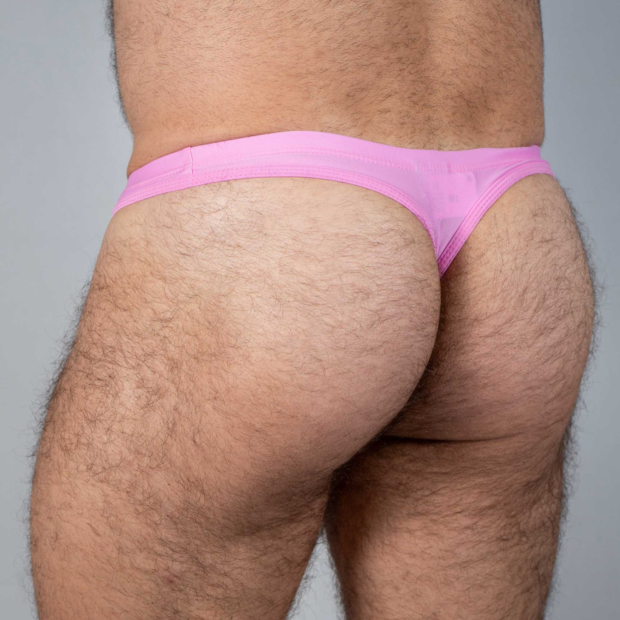 Pink tulio swim thong made of sheer fabric featuring a solid color design shown from the back side