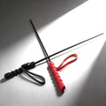 Two slim, black rods with textured handles (one black, one red) and matching wrist straps, crossed on a grey surface.