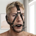 Strict Leather black leather ball gag head harness with metal hardware, worn on a man’s face.