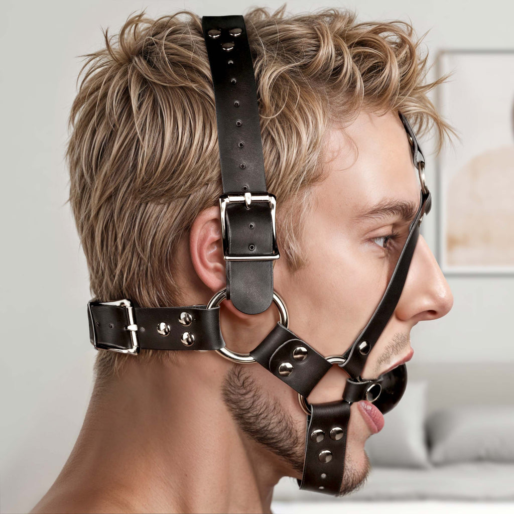 Strict Leather ball gag harness: black leather straps with silver buckles and hardware worn on a man’s head.
