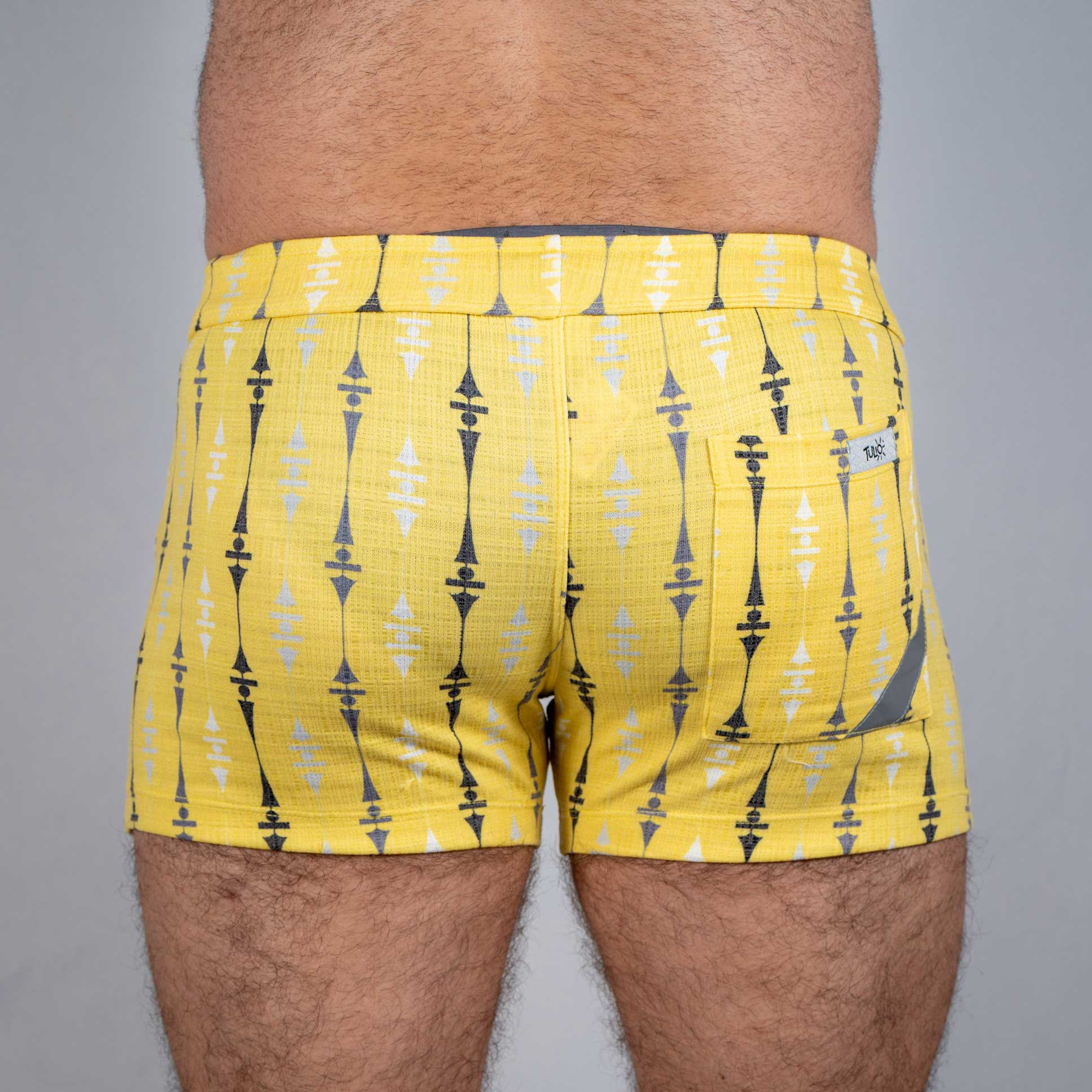 Bright yellow wallpaper print linen texture shorts with bold black and white geometric pattern and a back pocket tag visible