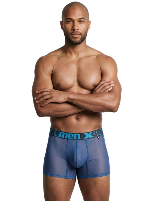 A model stands with arms crossed wearing blue mesh boxer briefs with a branded waistband.