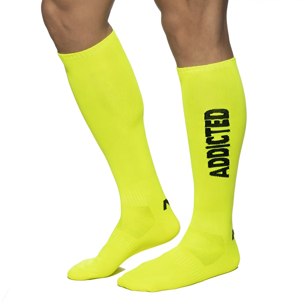 Bright neon yellow knee-high socks with bold black addicted lettering on the side for casual streetwear