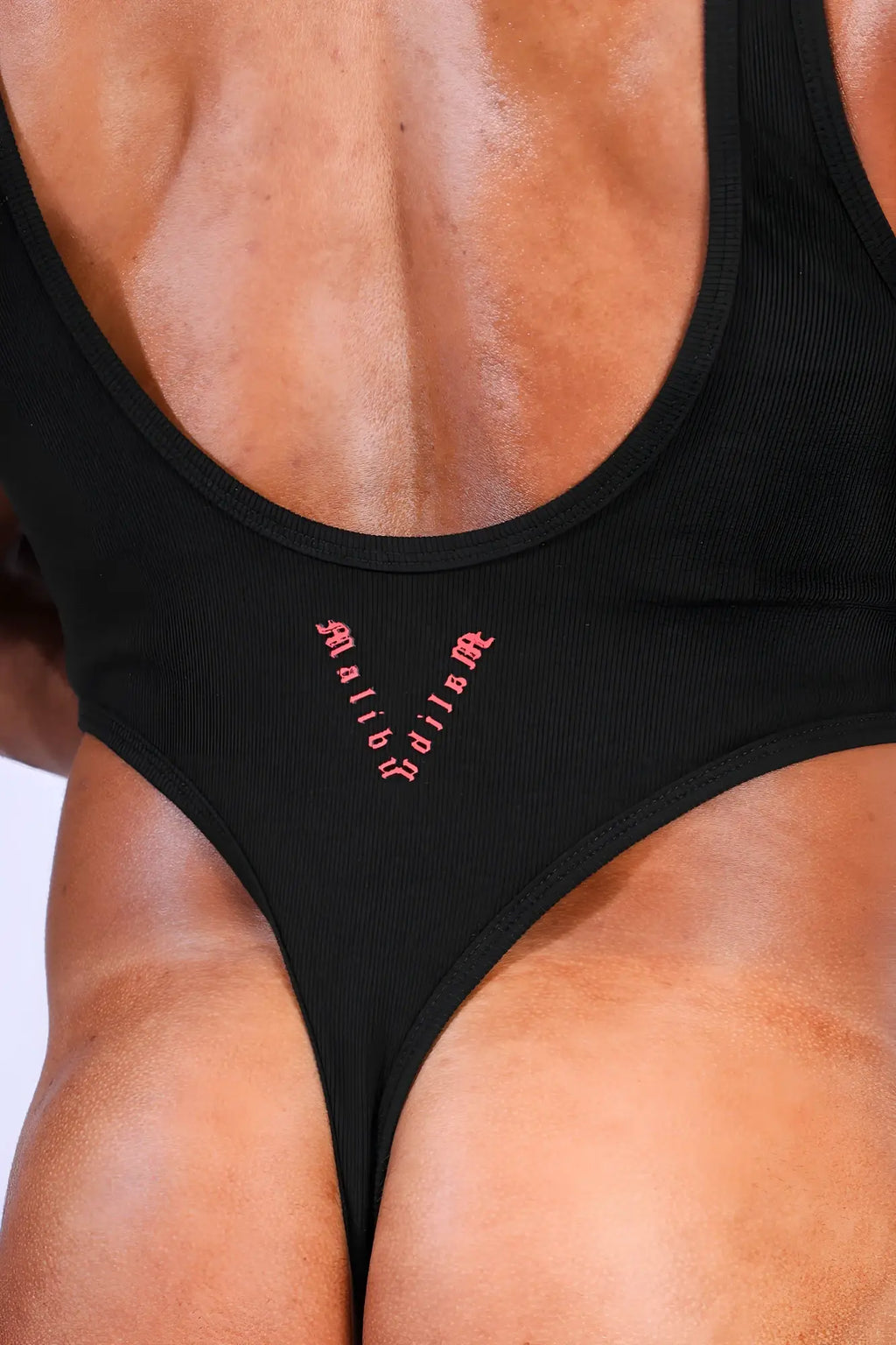 Back view of afterglow ribbed bodysuit black athletic-style one-piece with deep back cutout and pink malibu embroidery