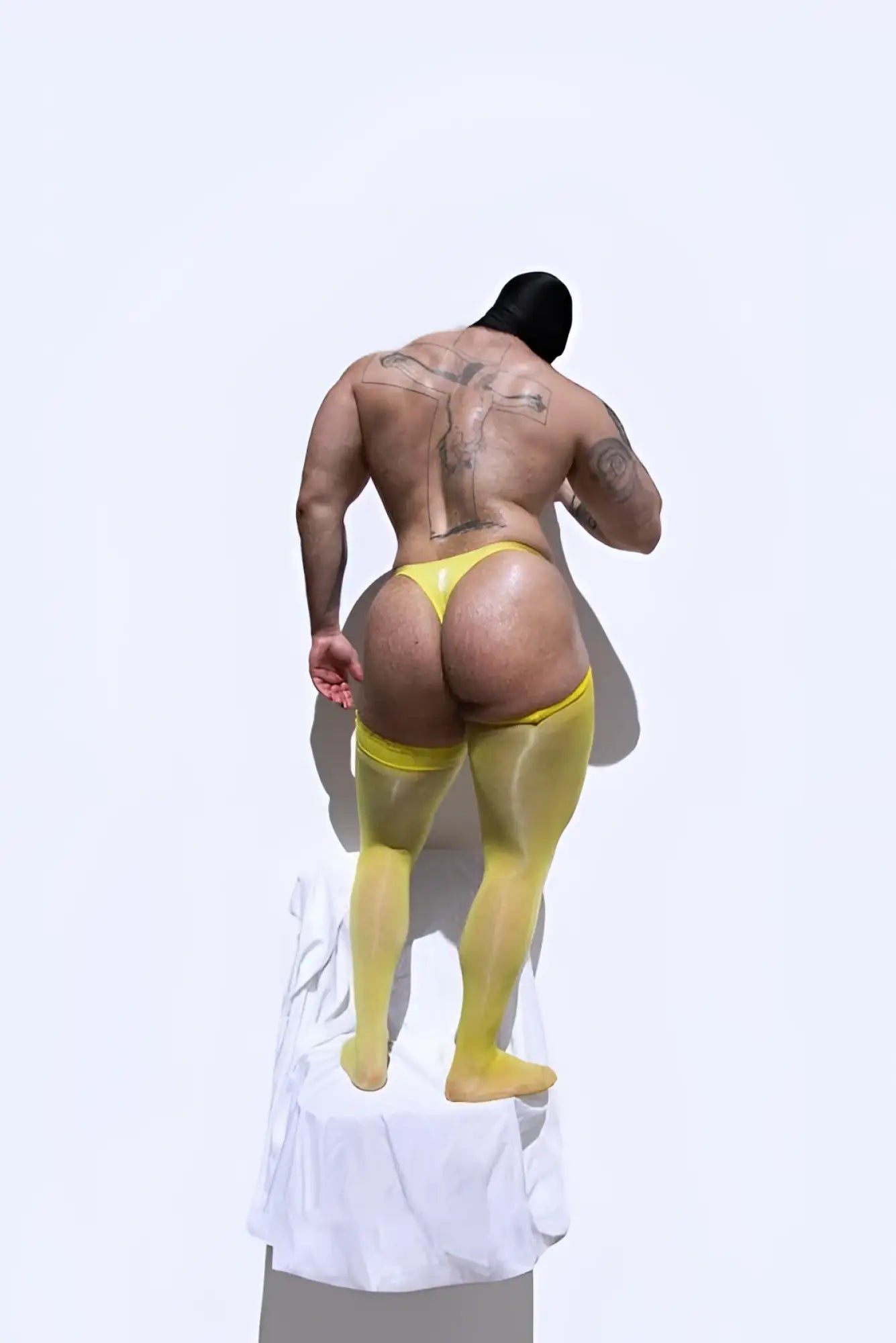 A muscular man wearing allure roll-up stockings in bright banana yellow sheer tights and matching underwear