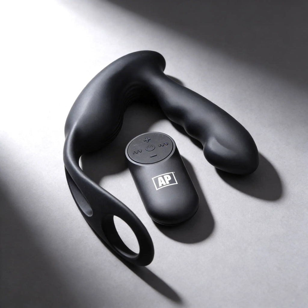 Alpha Pro 7X black silicone prostate stimulator and harness with a matching remote control on a grey surface.