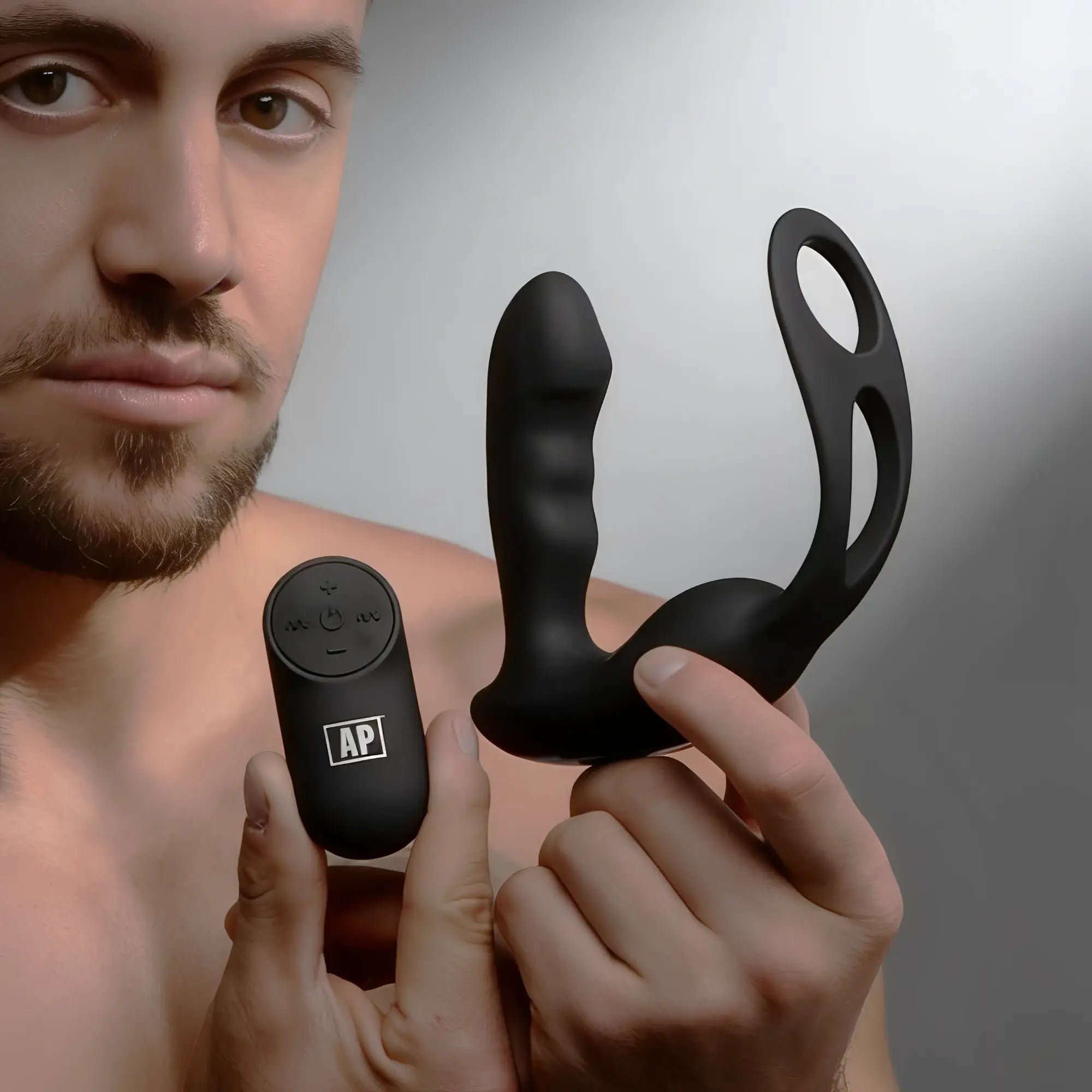 Alpha Pro 7X black silicone prostate stimulator with a cock and ball harness and remote control held by a man.