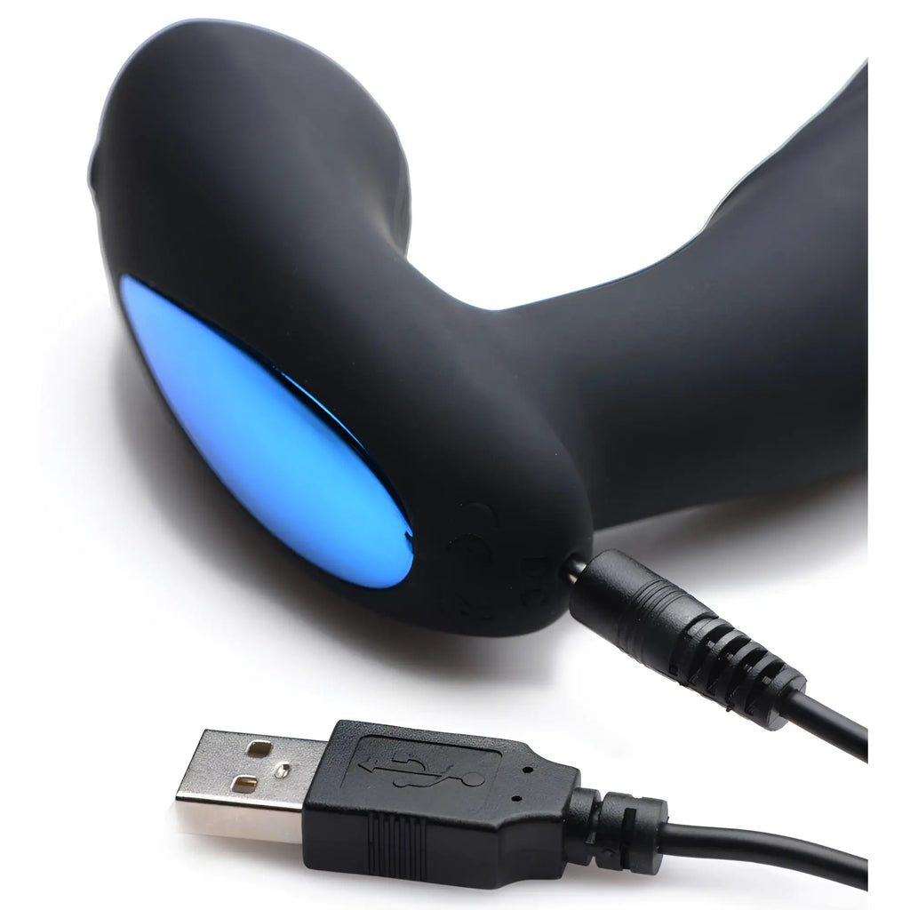 Alpha Pro 7X P-Thump prostate stimulator in matte black with a glowing blue light, connected to a USB charging cable.