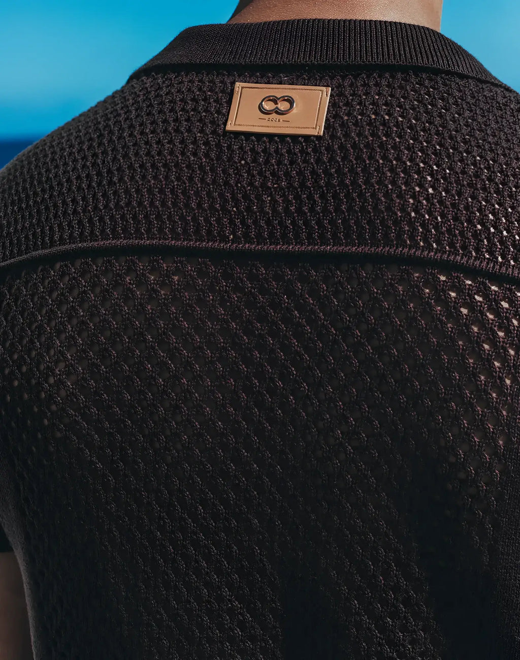 Amafi knit shirt is a black textured knit polo with a tan leather patch featuring an interlocking double-o logo