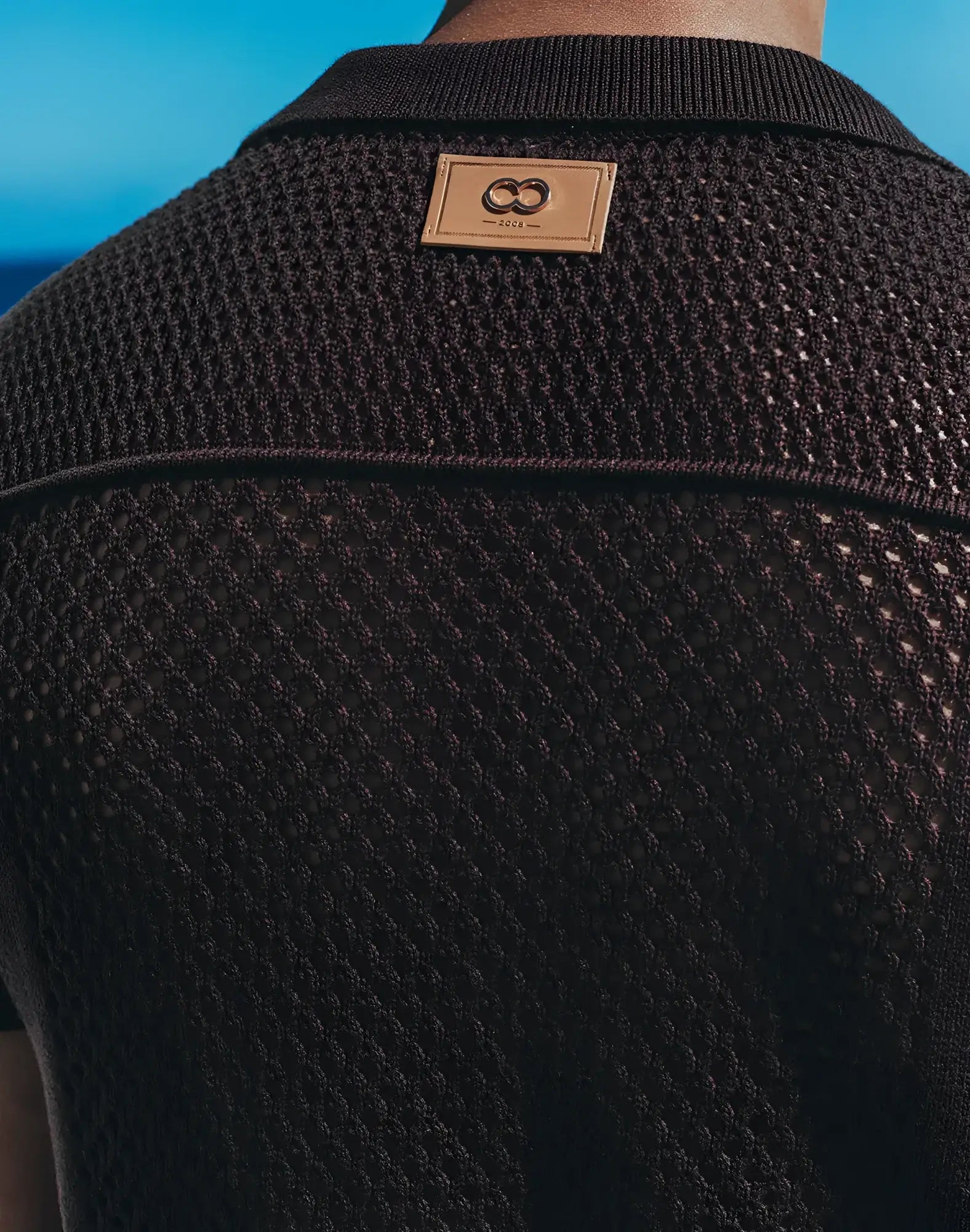 Amafi knit shirt is a black textured knit polo with a tan leather patch featuring an interlocking double-o logo