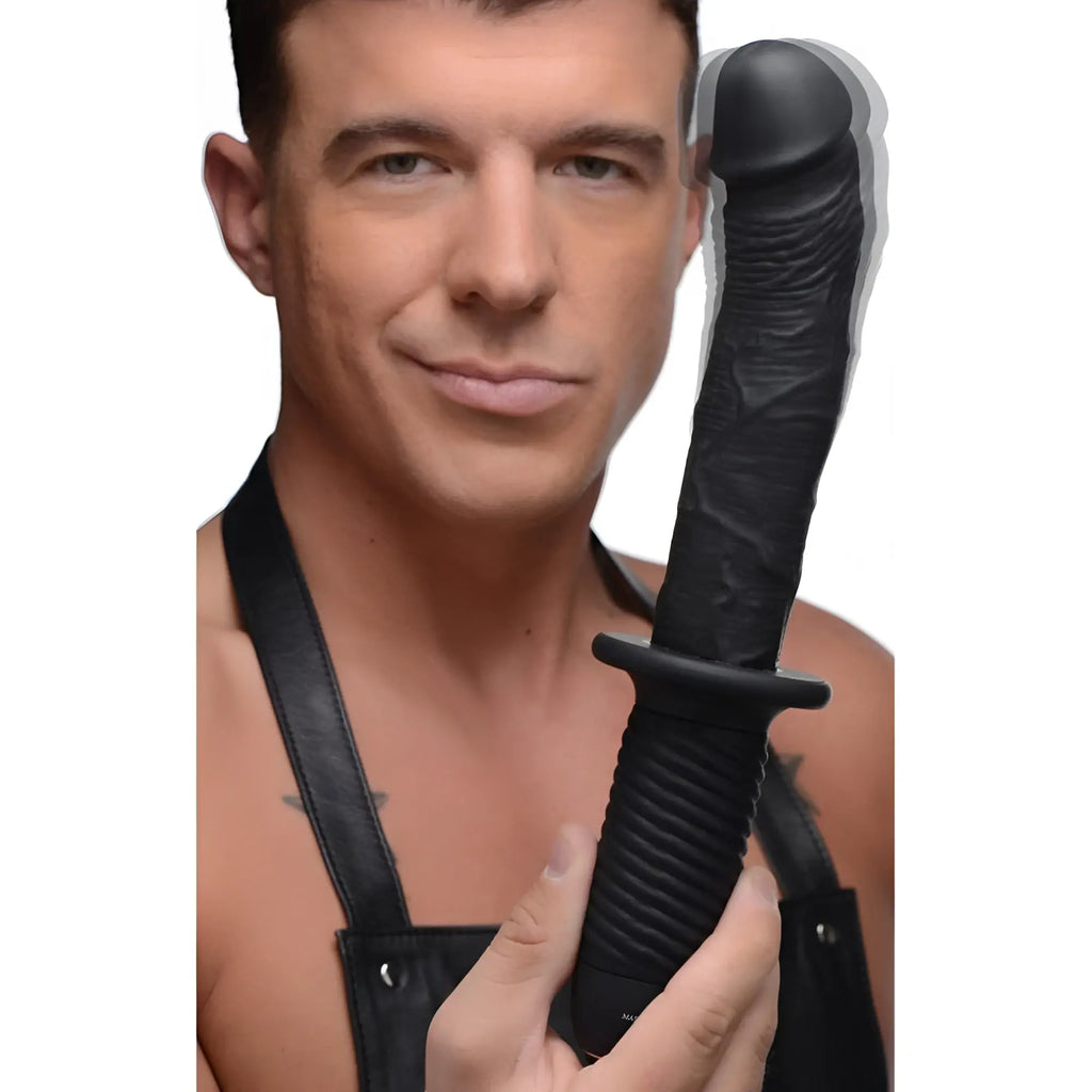 Man in leather apron holding a black, realistic Ass Thumpers silicone vibrating phallus with a ridged grip handle.