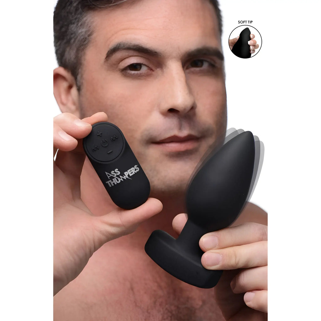 Man holding a smooth, black Ass Thumpers The Taper 10X vibrating butt plug and its matching remote control.