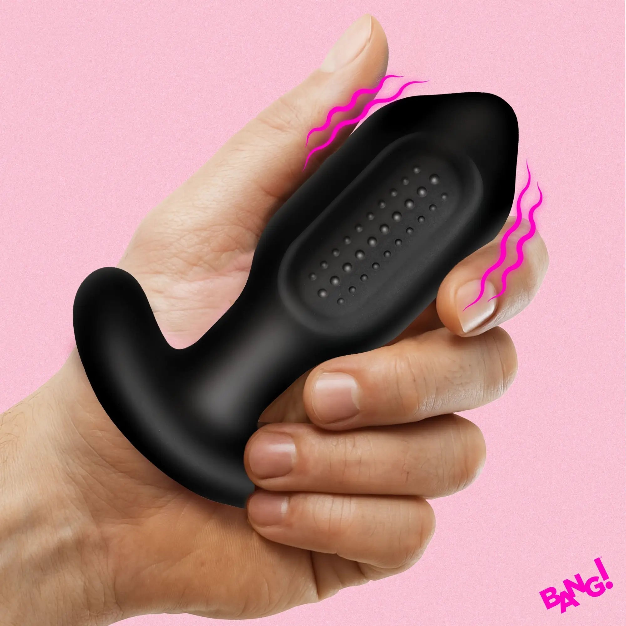 A hand holds a black, silicone Bang Bumpy Vibrating Butt Plug with a textured, dotted surface against a pink background.