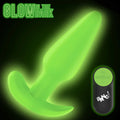 Bang Glow-in-the-Dark silicone butt plug with flared base and matching remote control, shown glowing green in the dark.