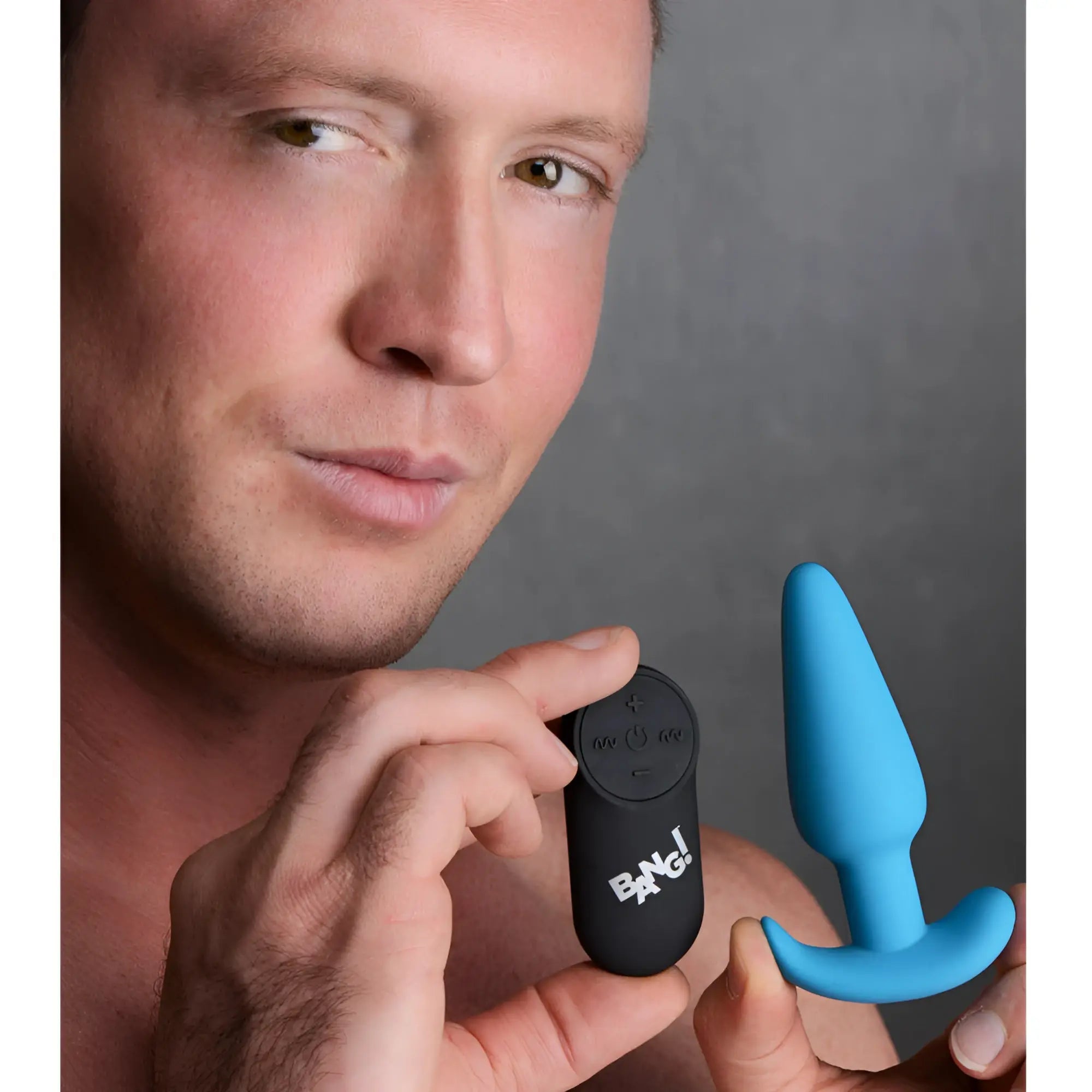 A man holds a blue Bang silicone vibrating butt plug next to its black, branded remote control.
