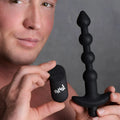 A man holds a black Bang vibrating silicone anal beads set and its matching wireless remote control.