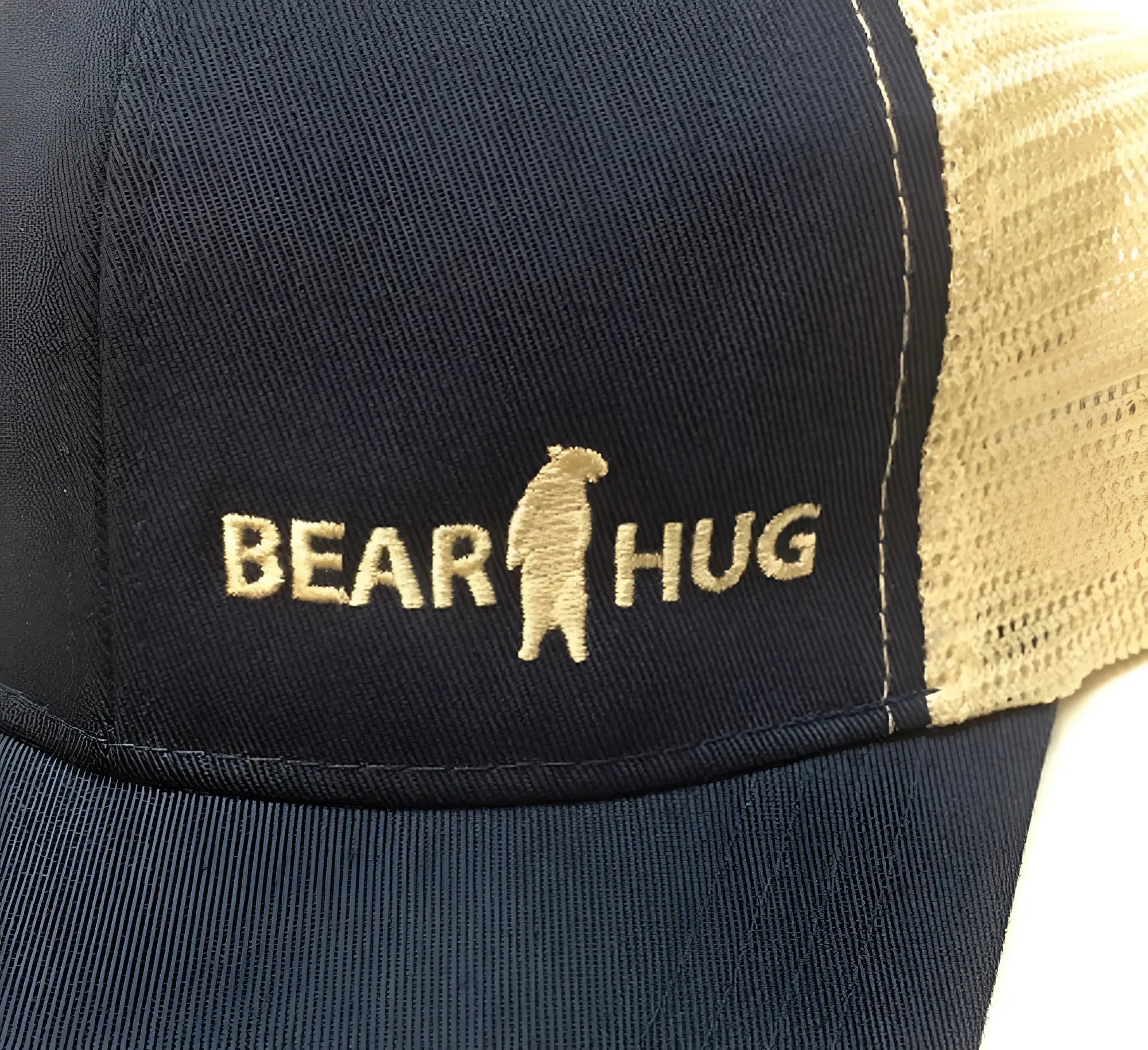Navy blue and tan trucker baseball cap with embroidered gold bear hug logo perfect for casual wear