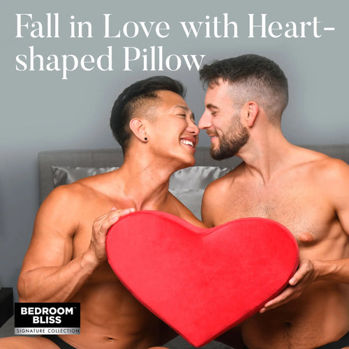 Bedroom Bliss The Heart Pillow: Two men smiling and holding a bright red, heart-shaped plush pillow in a bedroom.