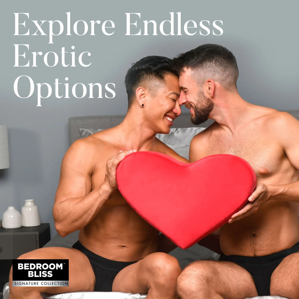 Two men in black underwear sitting on a bed holding a large, red Bedroom Bliss Heart Pillow.