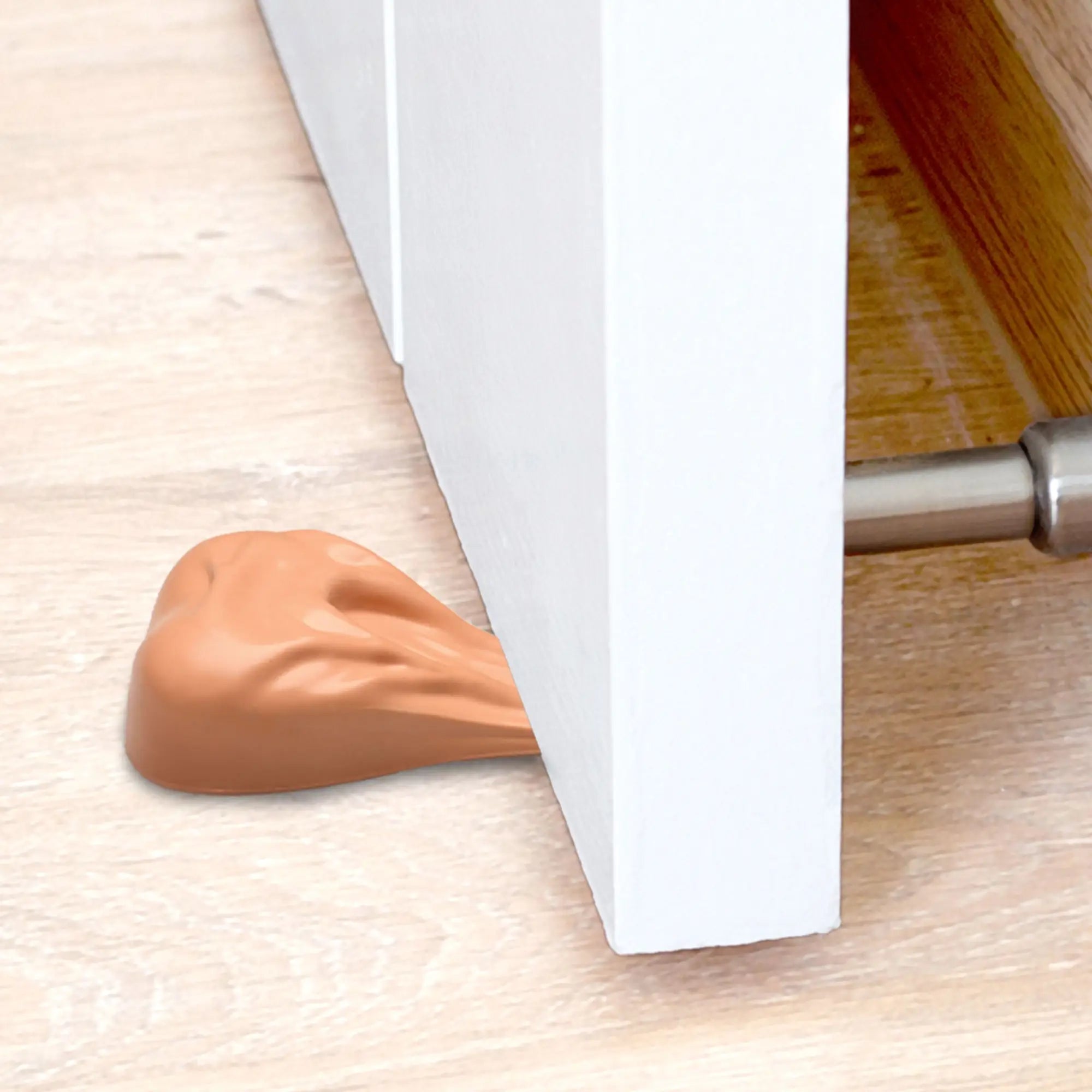 Big Ballers Big Balls door stop: a tan, anatomically shaped silicone wedge holding open a white door on a wood floor.