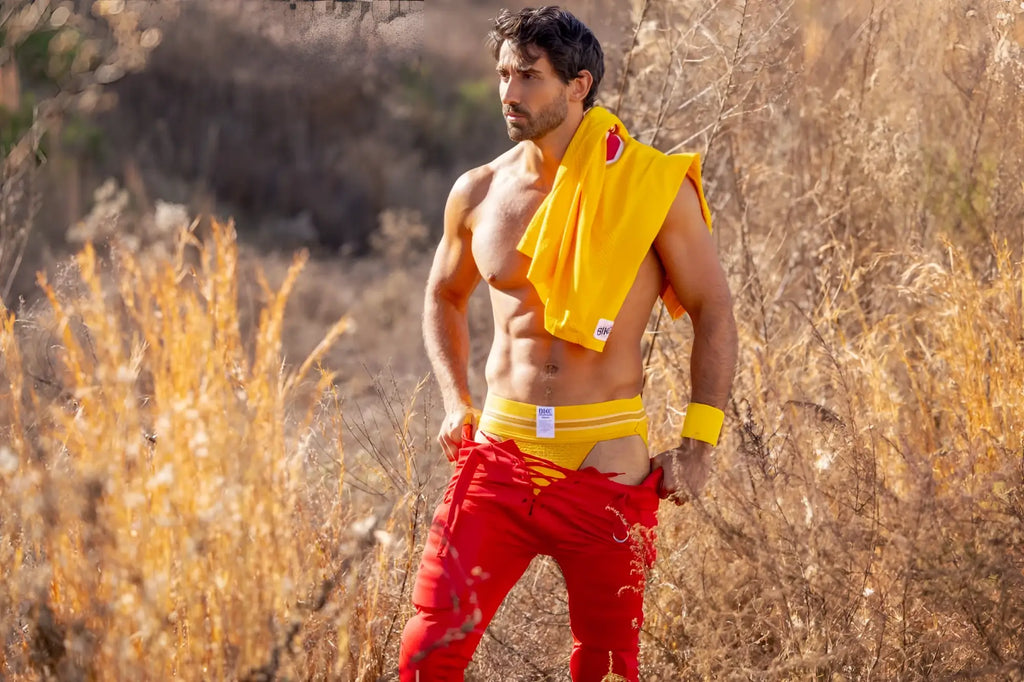 A man wearing bright red athletic pants with yellow trim and a yellow BIKE athletic jockstrap draped over his shoulder