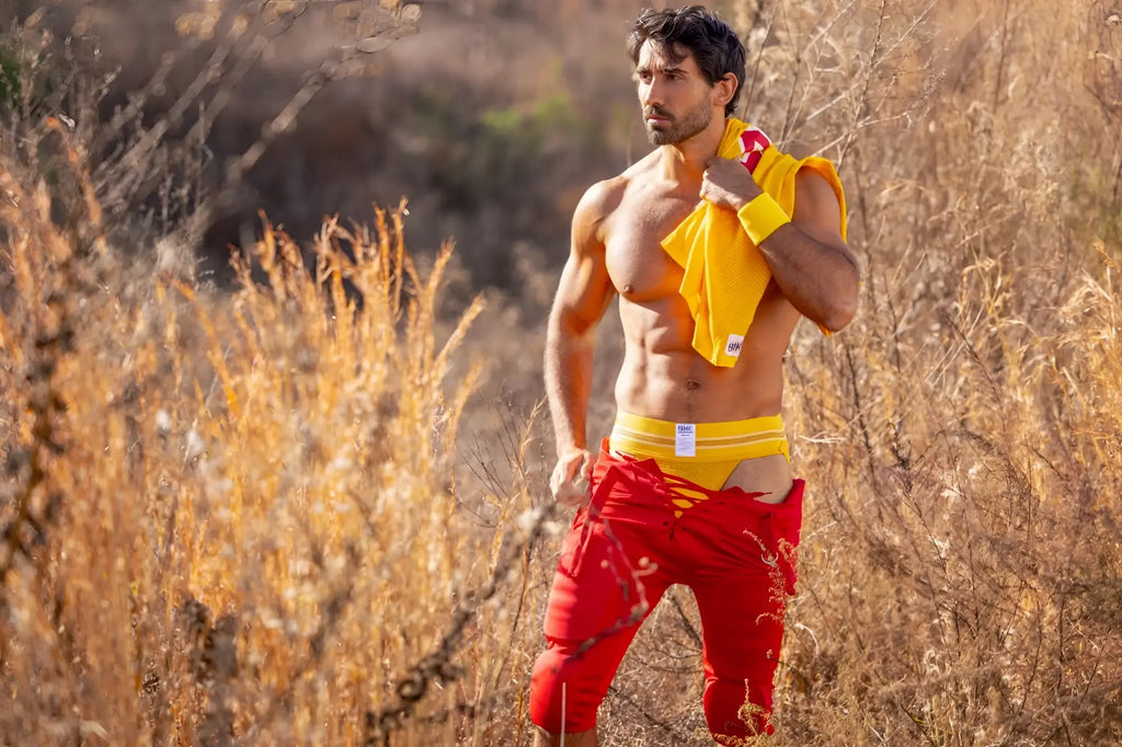 A man wearing a bright yellow bike athletic jockstrap with red torn fabric shorts visible from the front