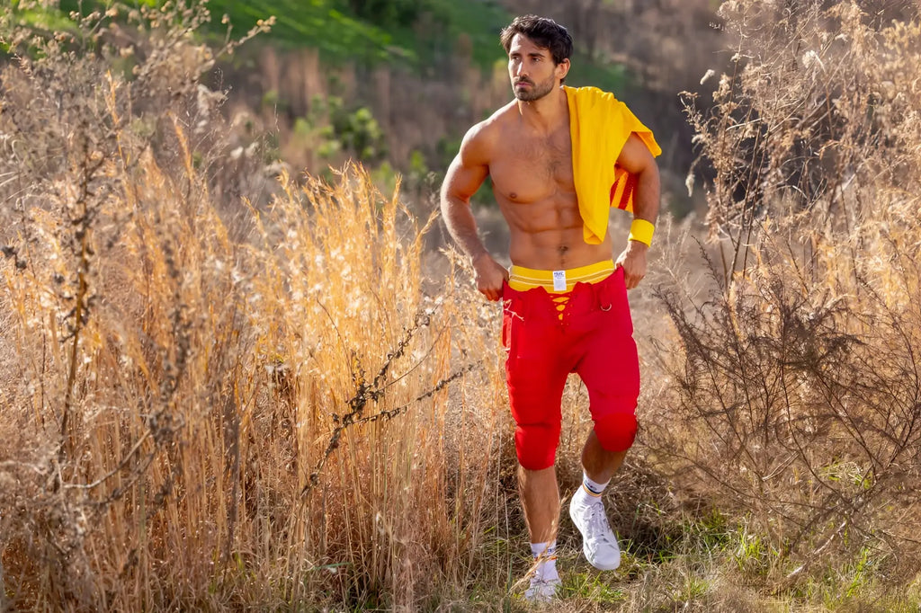 A muscular man wearing the yellow bike athletic bas306 original number 10 yellow jockstrap with red shorts and white sneakers