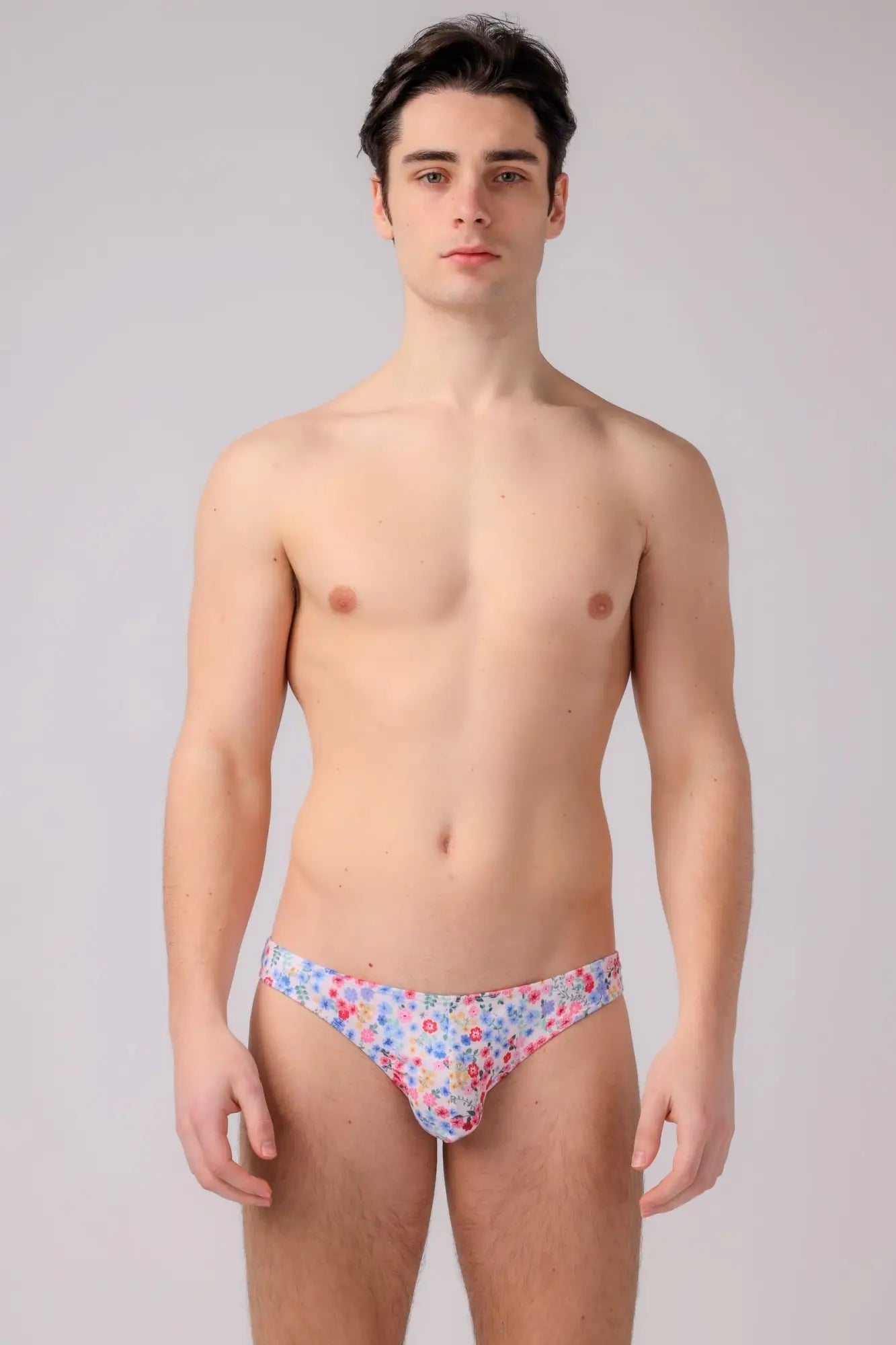 A man wearing floral-patterned bikini briefs with pink blue and white blossoms on a light background