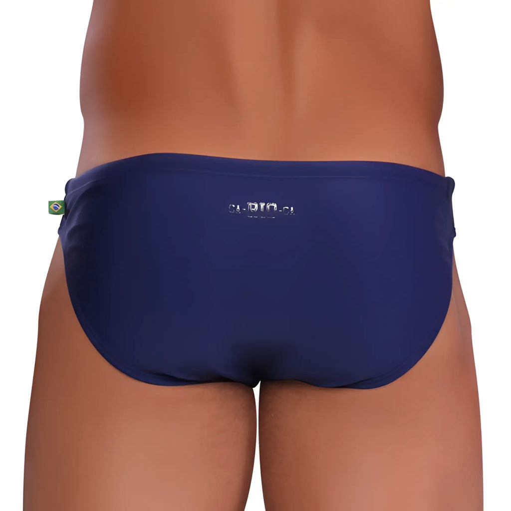 Back view of navy blue bikini cut solids colors sunga men’s swim trunks with brazilian flag tag and bio logo