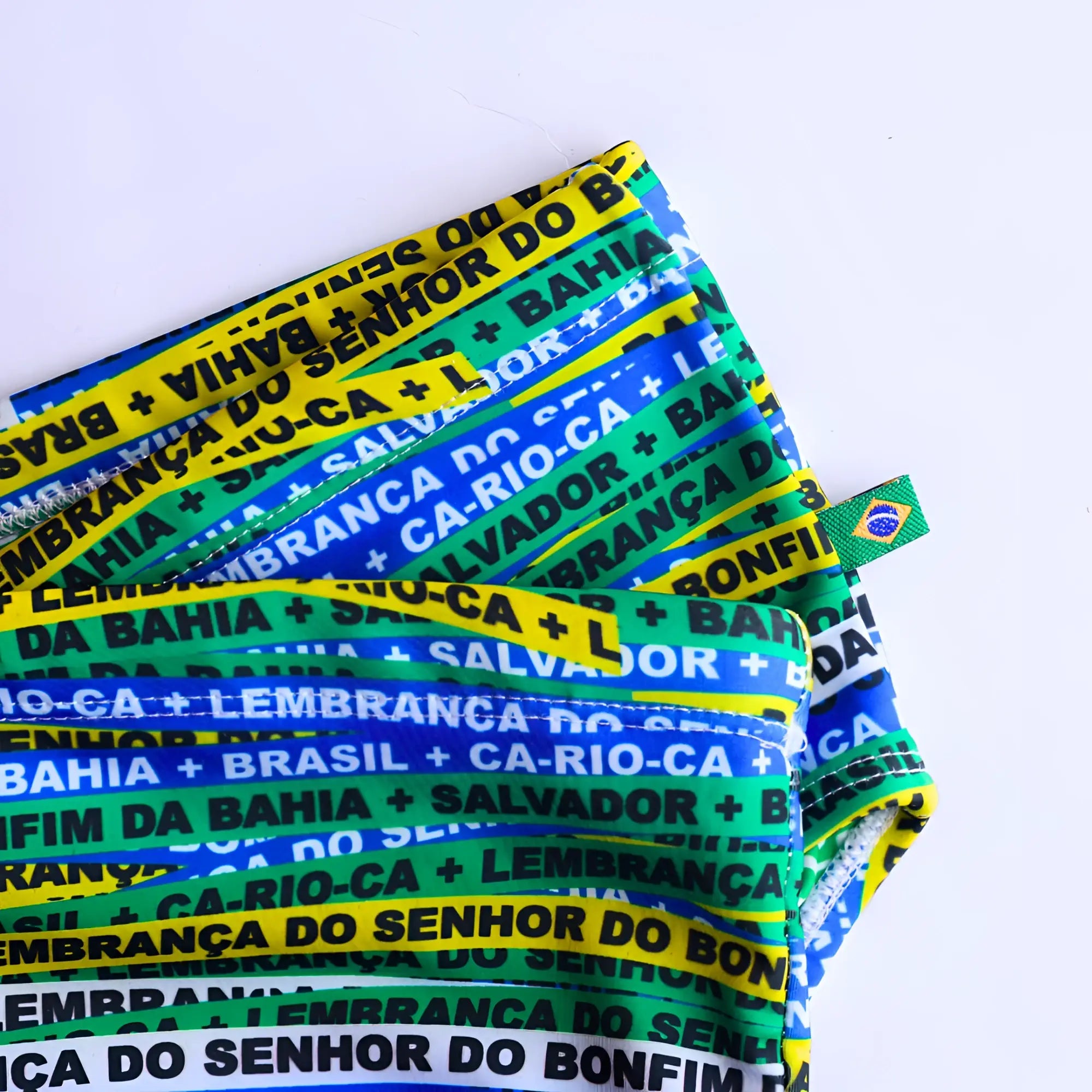 Brazilian-themed fabric pouch with bold green yellow and blue stripes and black repeating text for bonfim sunga swimwear