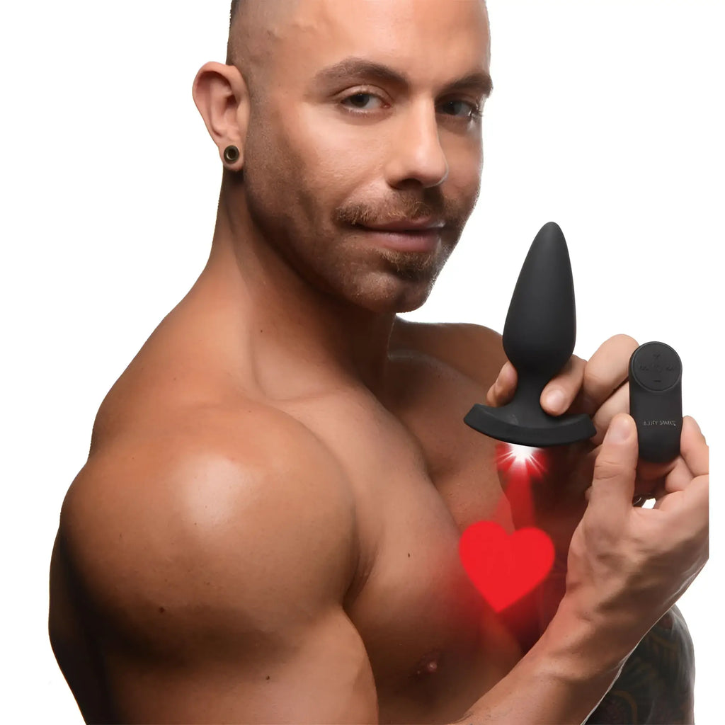 A man holding a black Booty Sparks laser heart silicone anal plug and remote, projecting a red heart light.