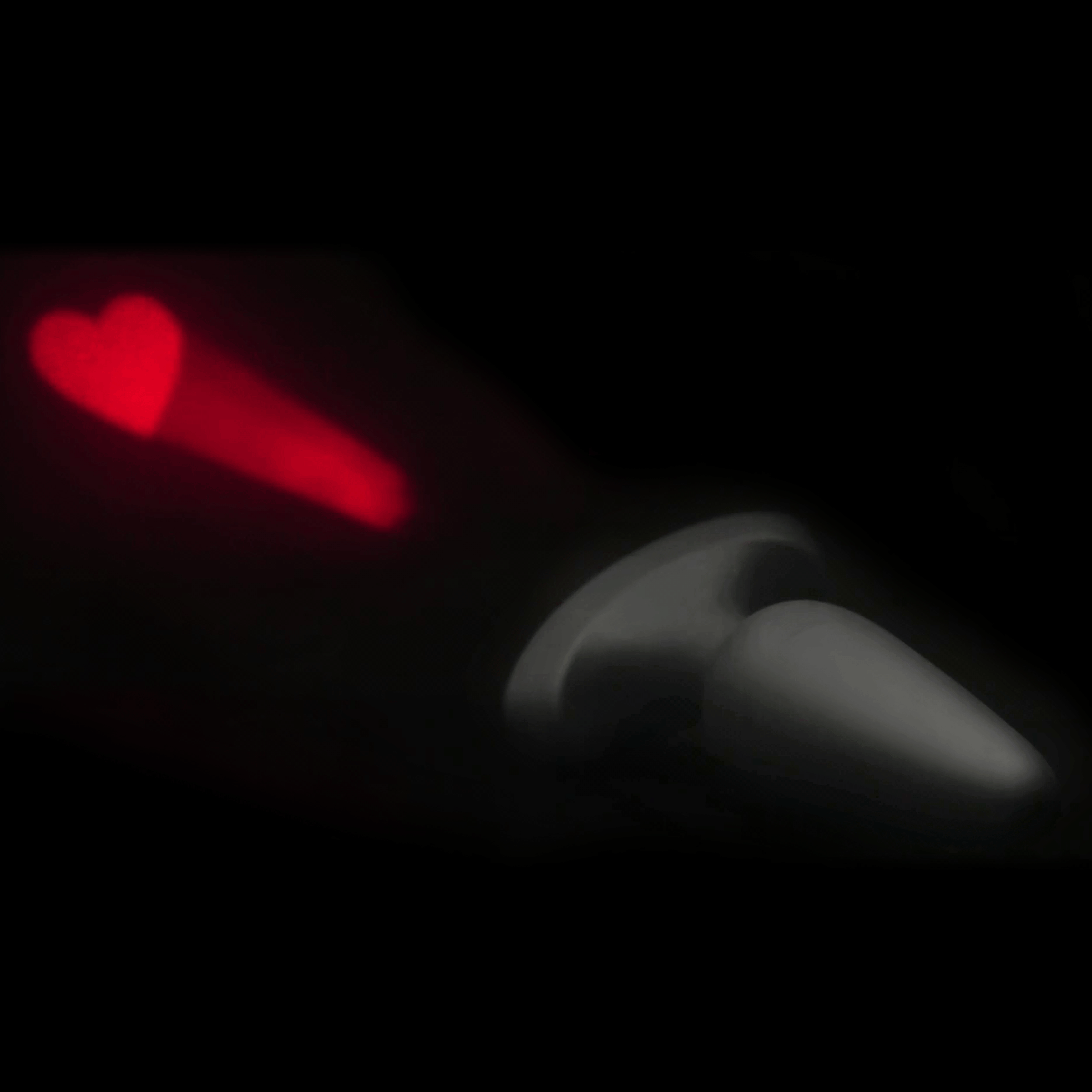 Booty Sparks 28X silicone anal plug projecting a bright red heart laser pattern against a dark background.