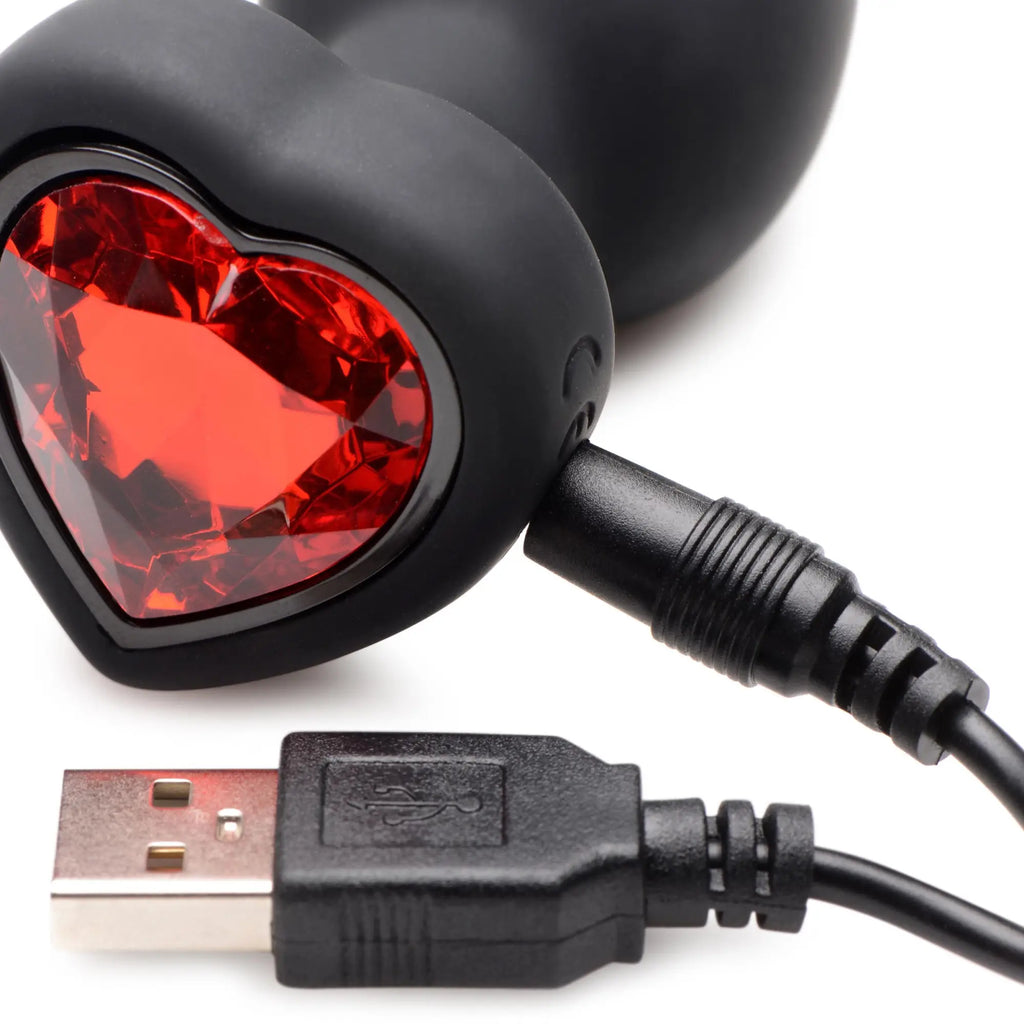 Booty Sparks 28X black silicone anal plug with a faceted red heart gem base and attached USB charging cable.