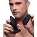 A person holds a black Booty Sparks 7X light-up anal plug and its matching wireless remote control.