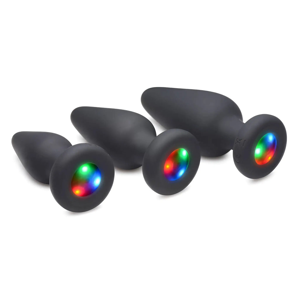 Three matte black Booty Sparks silicone anal plugs in increasing sizes, each featuring a glowing multi-colored LED base.