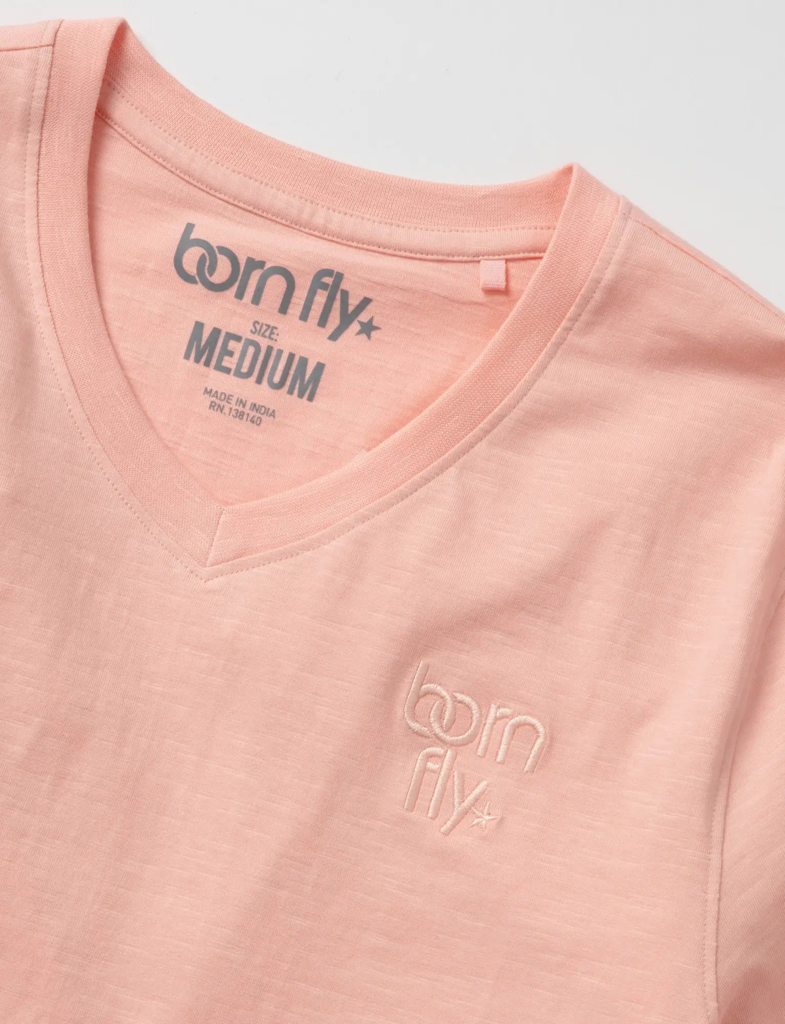 A soft peach-colored cotton born fly v-neck tee with subtle embroidery and brand tag at the neckline
