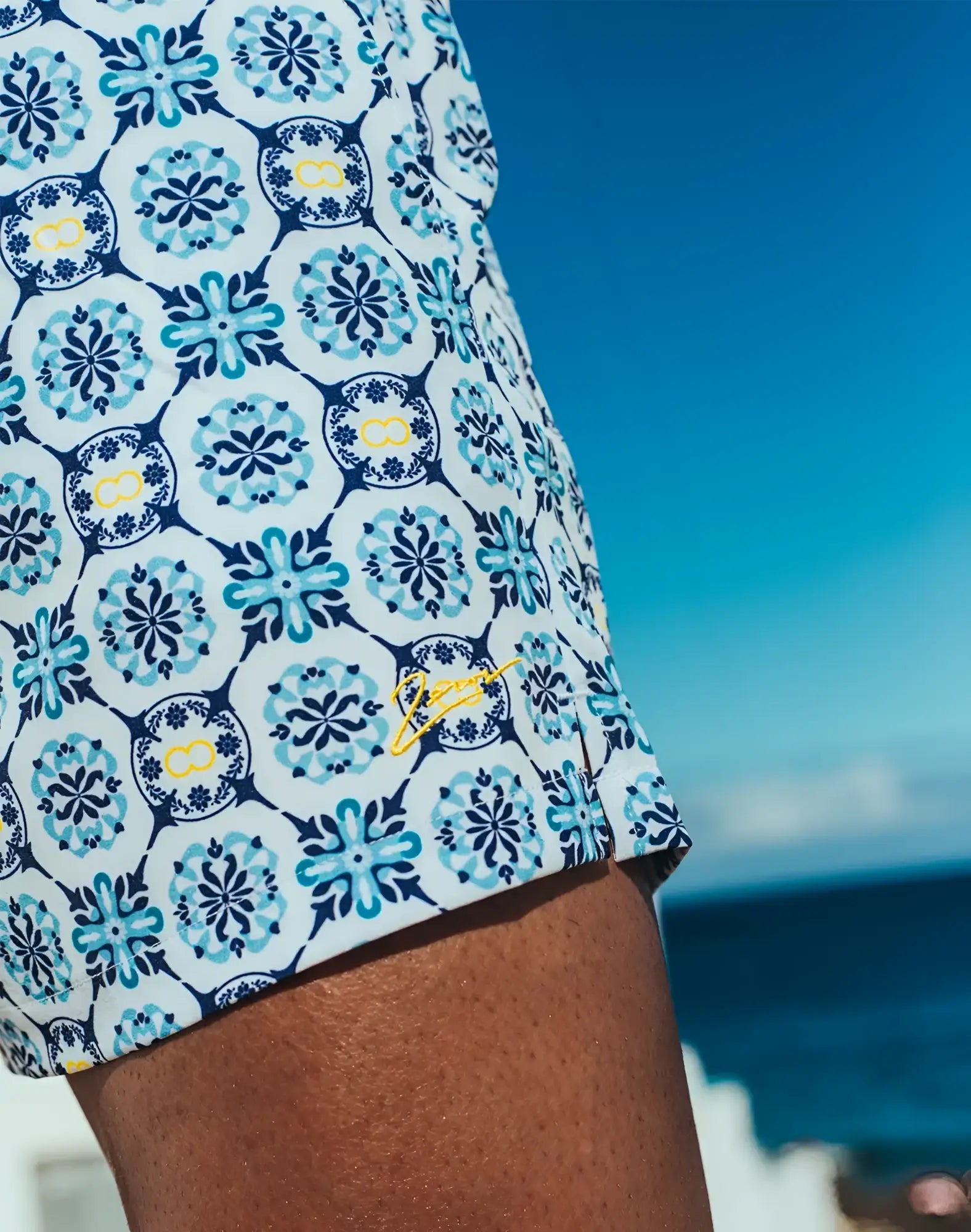 Byron swim short mykonos print white swim trunks with teal navy floral tile pattern yellow accents and side embroidered logo