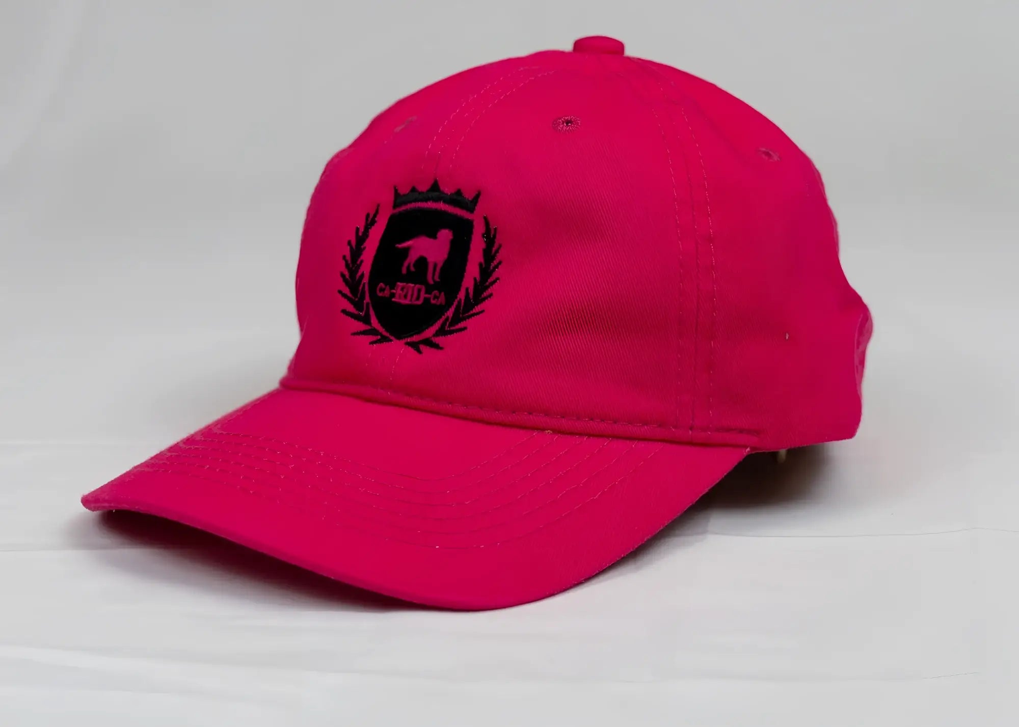 A vibrant pink ca-rio-ca designer dad hat with black embroidered dog crest and laurel wreath on the front