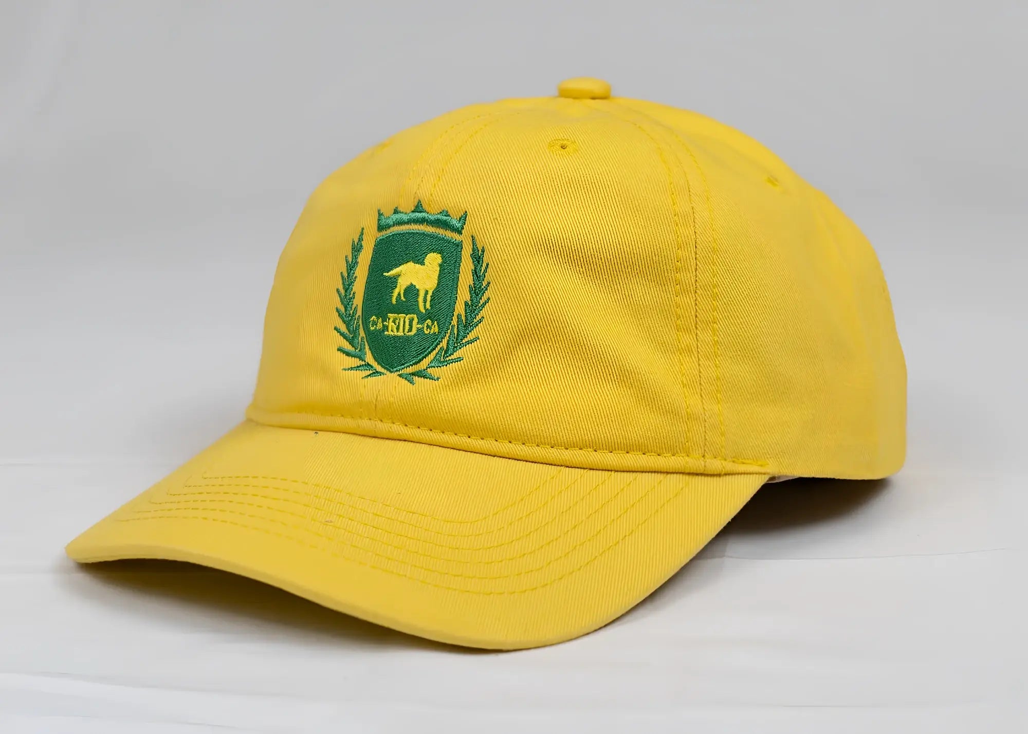Bright yellow ca-rio-ca men’s baseball cap with green embroidered dog crest and laurel wreath designer logo