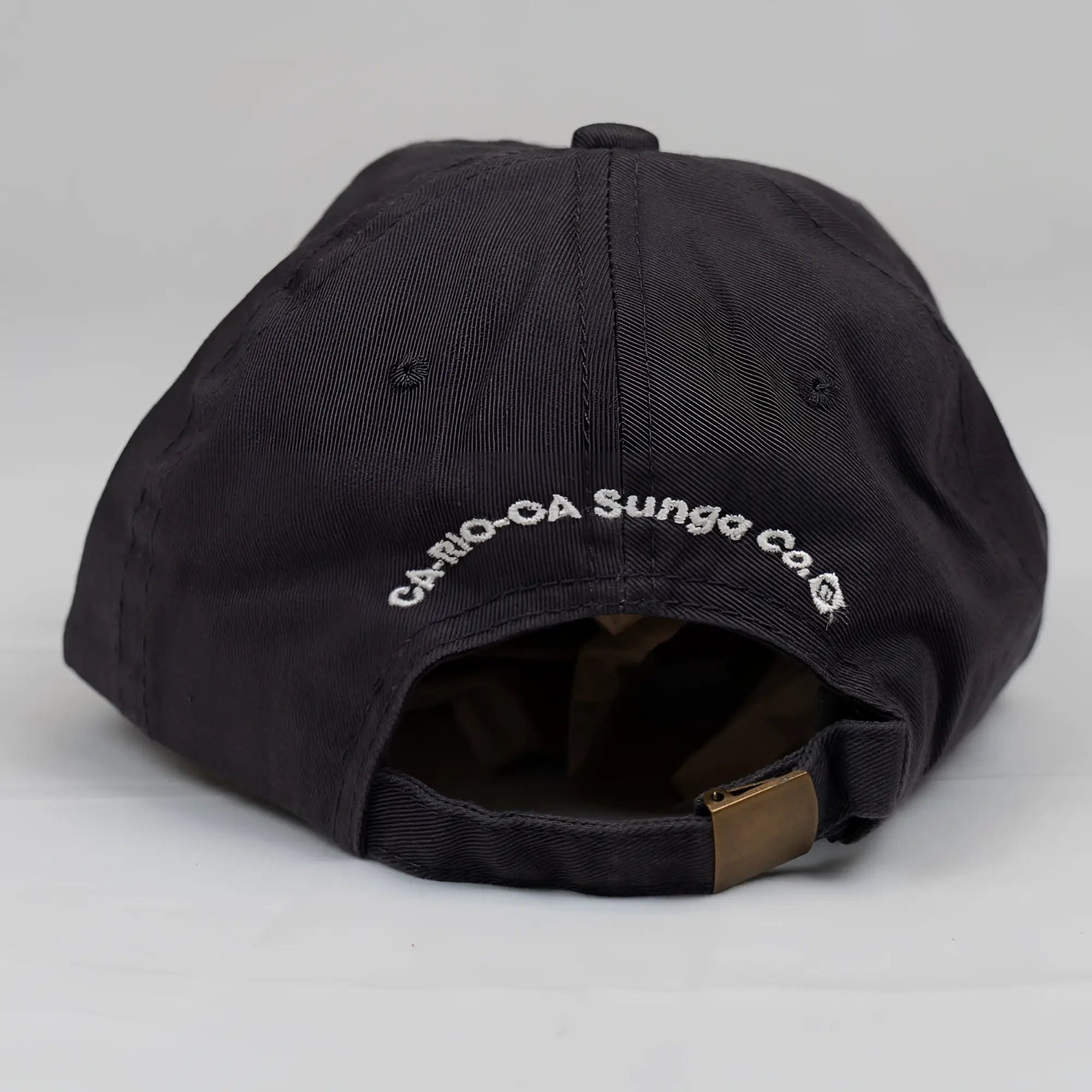Black cotton ca-rio-ca crest logo embroidered designer dad hat with white text and brass adjustable strap showing back side