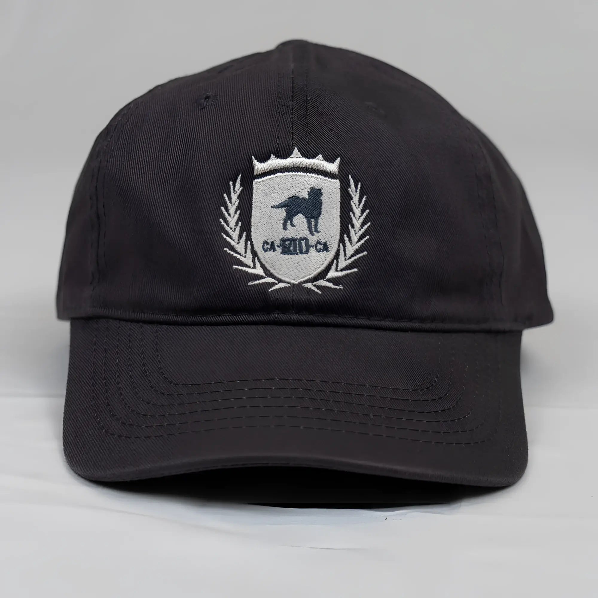 Black cotton dad hat with white embroidered CA-RIO-CA shield emblem featuring black dog and laurel wreath details