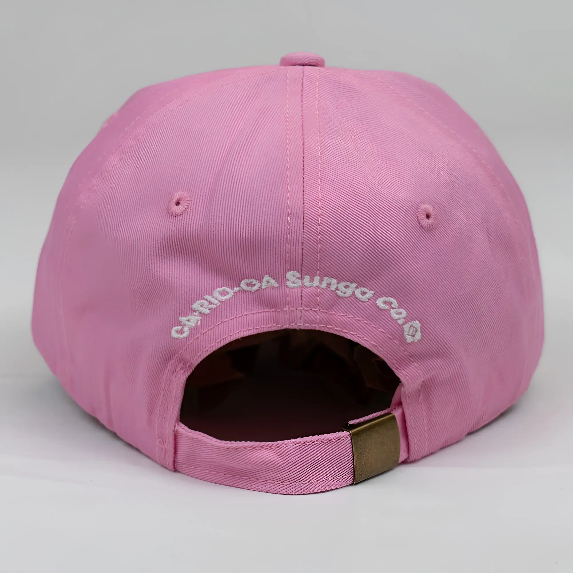 Pink cotton ca-rio-ca crest logo embroidered dad hat with white text and brass metal adjustment strap back side view